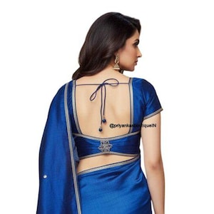 May include: A royal blue saree blouse with a low back and short sleeves. The blouse has a decorative design at the waist and a tie closure at the back. The saree is draped over the shoulder.