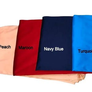 May include: Four fabric swatches in peach, maroon, navy blue, and turquoise. Each swatch has a label with its color name. The fabrics are folded and stacked, showcasing the different colors and textures.