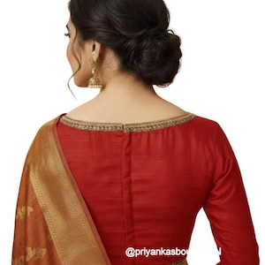 May include: A red long-sleeved blouse with a gold trim neckline and sleeve cuffs. The blouse is paired with a gold and orange patterned fabric. The text "@priyankasbo" is visible on the blouse.