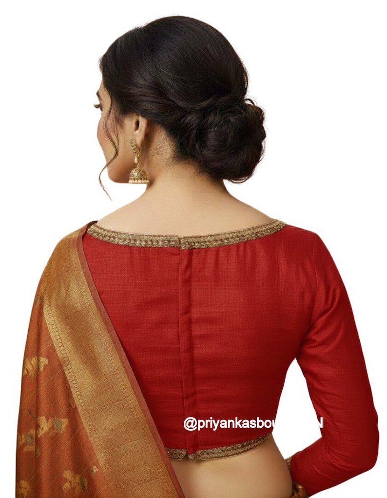 May include: A red long-sleeved blouse with a gold trim neckline and sleeve cuffs. The blouse is paired with a gold and orange patterned fabric. The text "@priyankasbo" is visible on the blouse.