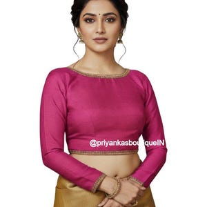 May include: A magenta long-sleeve blouse with gold trim around the neckline and cuffs. The blouse has a round neckline and is paired with a gold-colored skirt. The text "@priyankasboutiqueN" is visible on the blouse.