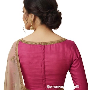 May include: A magenta-colored blouse with long sleeves and a boat neckline, trimmed with gold embroidery. The back of the blouse is visible, with a central seam. A portion of a beige sari with gold embroidery is also visible.