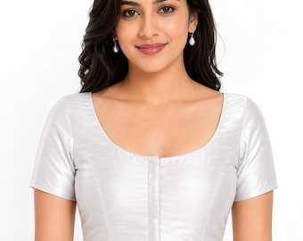 May include: A silver-colored, short-sleeved blouse with a scoop neckline and a button-up front. The blouse has a subtle sheen and is worn by a person. The text "@PriyankasBoutiqueIN" is visible at the bottom.
