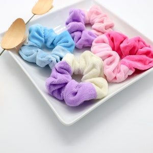 May include: A set of six colorful scrunchies on a white plate. The scrunchies are made of soft, fuzzy fabric and come in a variety of colors, including pink, blue, purple, and white.