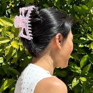 May include: A pink plastic hair claw with a textured surface, holding a woman's dark hair in a bun.