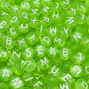 May include: A close-up of a large pile of lime green alphabet beads. The beads are made of plastic and have white letters on them.