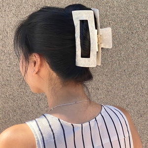 May include: A white plastic hair claw with a rectangular shape and a smooth, glossy finish. The claw is designed to hold hair in place and is a popular accessory for women.