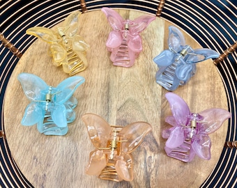 May include: Six butterfly-shaped hair clips in various pastel colors, including pink, blue, and yellow. The clips are made of plastic and have a gold-colored metal clasp.