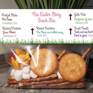 May include: A clear plastic bag filled with a variety of snacks, including pretzels, crackers, goldfish crackers, and marshmallows. The bag is labeled with a colorful tag that reads "The Easter Story Snack Mix" and includes Bible verses related to the Easter story.