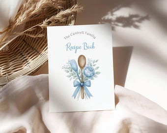 May include: A white recipe book with the text "The Cantrell Family Recipe Book" in blue script. The cover features a watercolor illustration of a wooden spoon, spatula, blue flowers, and a blue ribbon.