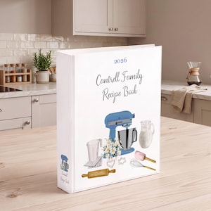 Puede incluir: Una carpeta de tres anillas blanca titulada 2026 Cantrell Family Recipe Book. La portada presenta ilustraciones en acuarela de una batidora de pie azul, una jarra de leche, un rodillo, un batidor, una espátula, moldes y margaritas blancas.