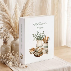 May include: A white three-ring binder with the text My Favorite Recipes printed on the front cover. The cover features a watercolor illustration of a ceramic pitcher, a bowl, a basket of bread, and kitchen utensils with green foliage.