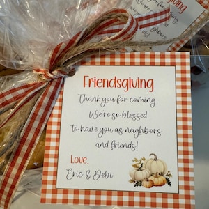 May include: A gift basket wrapped in cellophane, tied with a red and white checked ribbon and twine. The gift tag reads "Friendsgiving" and includes a message of thanks and a pumpkin illustration.