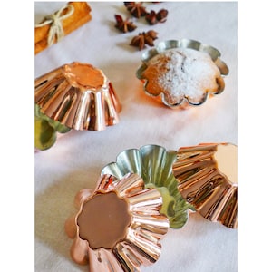 May include: Five copper-coloured baking cups with fluted edges. One cup is filled with a baked good topped with powdered sugar.