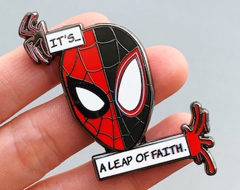 Könnte beinhalten: Ein Spider-Man-Emaille-Pin mit der Maske der Figur, rot und schwarz geteilt. Der Pin enthält den Text "IT'S..." und "A LEAP OF FAITH." Zwei silberne Spinnenakzente befinden sich auf beiden Seiten der Maske.