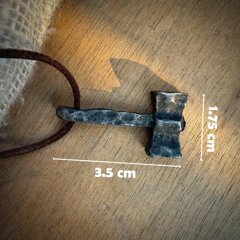 May include: A black metal hammer pendant with a 3.5 inch long handle and a 1.75 inch wide head. The pendant is on a brown leather cord.