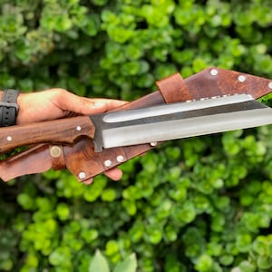K&ouml;nnte beinhalten: Eine braune Lederscheide mit einem silbernen Messer mit einem Holzgriff. Das Messer ist scharf und hat eine gebogene Klinge.