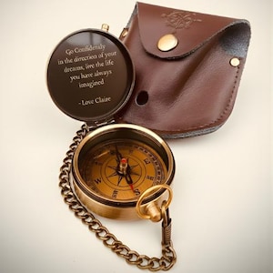 May include: A brass compass with a chain, open to show the quote: "Go Confidently in the direction of your dreams, live the life you have always imagined - Love Claire." It is accompanied by a brown leather case with a snap closure.