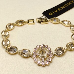 May include: Gold-toned bracelet with oval-shaped crystals and a central circular design with smaller pink crystals. The bracelet has a clasp closure and a Givenchy tag.