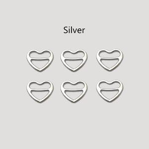 May include: Six silver heart-shaped charms with a cutout design. The word "Silver" is above the charms. These charms are suitable for jewellery making or craft projects.
