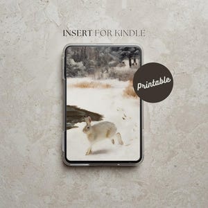 Puede incluir: Funda transparente para Kindle con un diseño de paisaje invernal que presenta un conejo blanco corriendo por la nieve. La funda tiene el texto "INSERT FOR KINDLE" en la parte superior y un círculo marrón con la palabra "Printable".