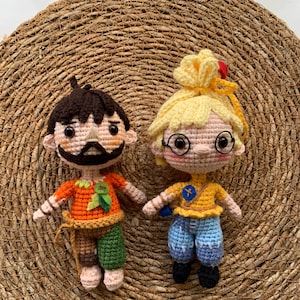 Op de afbeelding: Twee gehaakte poppen, een met bruin haar en een baard die een oranje shirt en een groene broek draagt, de andere met blond haar en een bril die een geel shirt en een blauwe broek draagt.