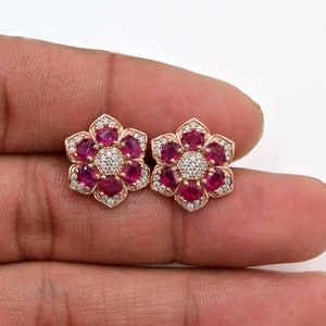 Op de afbeelding: Een paar roosgoudkleurige oorbelletjes in de vorm van een bloem met rode robijn en witte diamant accenten.