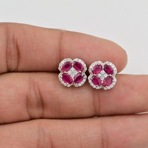 May include: A pair of silver earrings with a flower design. The earrings are set with red rubies and clear diamonds.