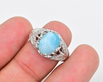 May include: A silver ring with a blue oval gemstone set in a leaf-shaped design. The ring is adorned with small clear stones.