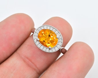 May include: A silver ring with a large oval-shaped orange gemstone surrounded by smaller clear gemstones.