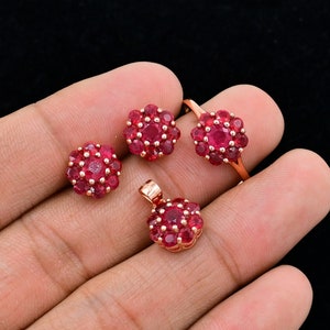 May include: A set of ruby jewelry featuring a ring, a pendant, and a pair of earrings. Each piece is adorned with a cluster of red rubies set in a floral design.