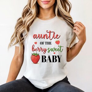May include: White t-shirt with the text "auntie of the berry sweet BABY" in red, green, and black. The design includes strawberry illustrations. A casual, everyday tee.