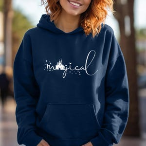 Puede incluir: Sudadera con capucha azul marino con la palabra "magical" en escritura blanca. La palabra "magical" va acompa&ntilde;ada de una silueta de castillo y estrellas. La sudadera tiene un bolsillo delantero y una capucha con cord&oacute;n.