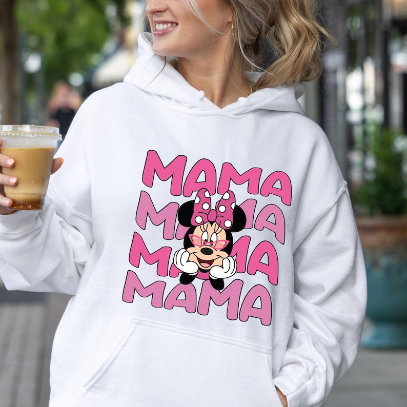 以下が含まれることがあります： ミニーマウスのピンクのグラフィックと「MAMA」という単語が3回繰り返された白いフーディーです。