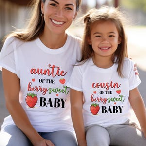May include: Two white t-shirts with matching text and graphics. One shirt says "auntie of the berry sweet BABY" with a strawberry graphic. The other says "cousin of the berry sweet BABY" with a strawberry graphic.
