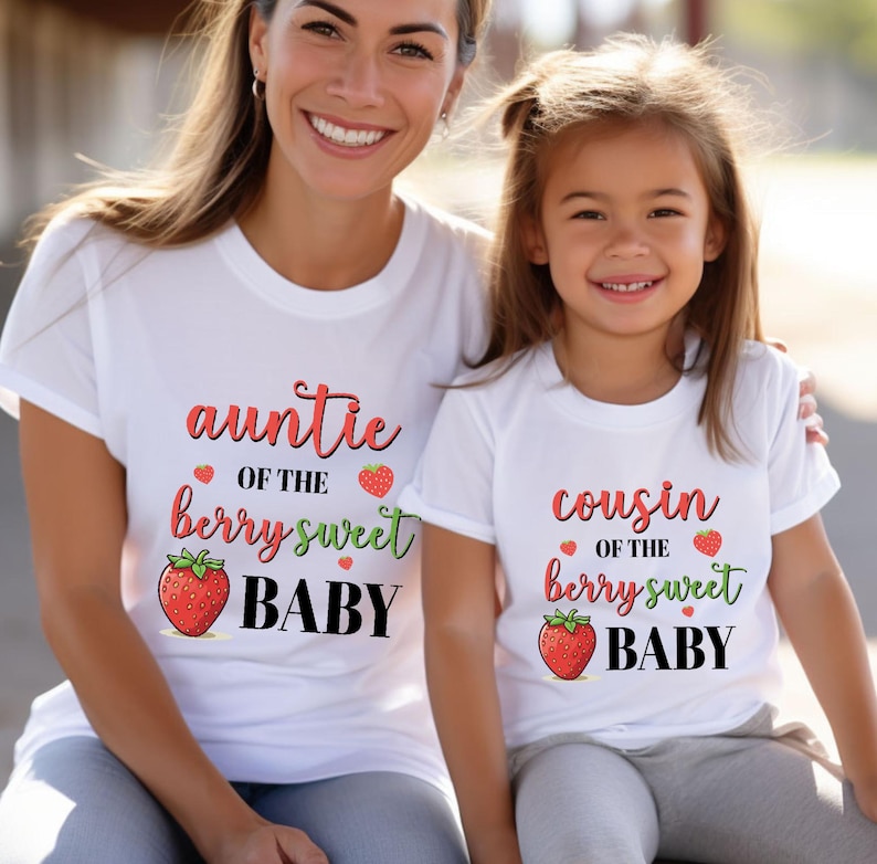 May include: Two white t-shirts with matching text and graphics. One shirt says "auntie of the berry sweet BABY" with a strawberry graphic. The other says "cousin of the berry sweet BABY" with a strawberry graphic.
