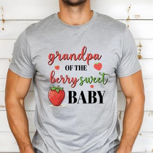 May include: A gray t-shirt with the text "grandpa of the berry sweet BABY" in red, green, and black. The design includes strawberry illustrations. The shirt is made of a soft material.