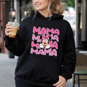 以下が含まれることがあります： ミニーマウスのピンクと白のグラフィックと「MAMA」という文字が4回繰り返された黒いフード付きスウェットシャツです。