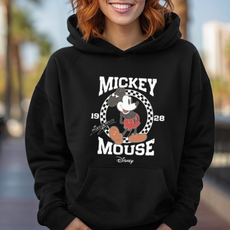 Puede incluir: Sudadera con capucha negra con un gr&aacute;fico blanco de Mickey Mouse en un c&iacute;rculo con el texto "Mickey Mouse" y "1928" a cada lado del c&iacute;rculo. El gr&aacute;fico tiene un aspecto vintage.