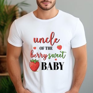 May include: White t-shirt with the text "uncle of the berry sweet BABY" in red, green, and black. The design includes strawberry illustrations. A casual tee for an uncle.