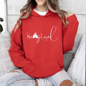Puede incluir: Sudadera roja con capucha con la palabra "magical" en escritura blanca. La palabra "magical" va acompa&ntilde;ada de un castillo blanco y estrellas. La sudadera tiene un bolsillo delantero y una capucha con cord&oacute;n.