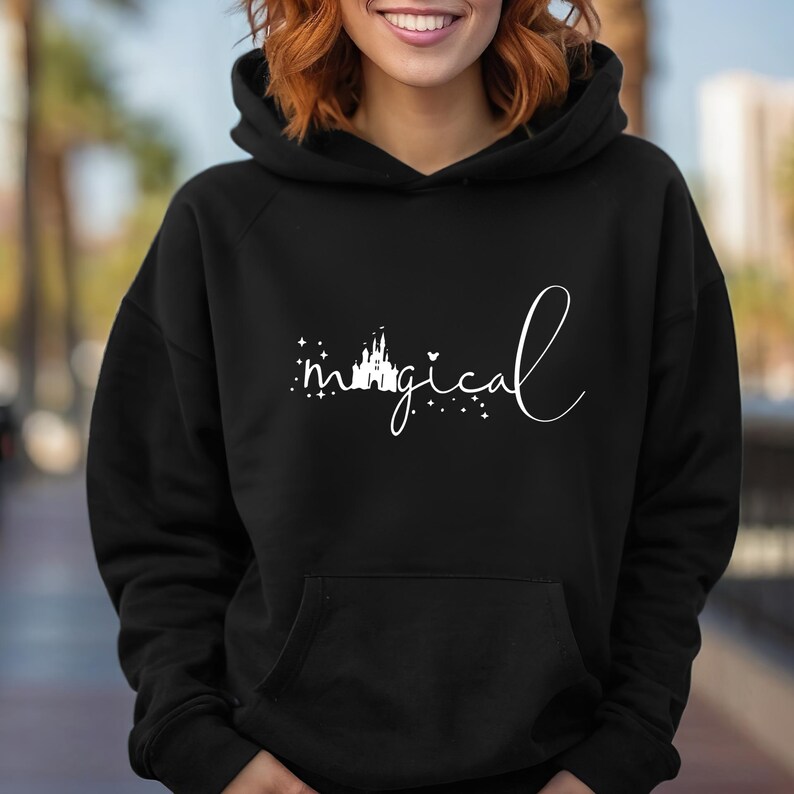 Puede incluir: Sudadera con capucha negra con la palabra "magical" en escritura blanca. La palabra "magical" est&aacute; acompa&ntilde;ada de una silueta de castillo y estrellas. La sudadera tiene un bolsillo delantero y una capucha con cord&oacute;n.