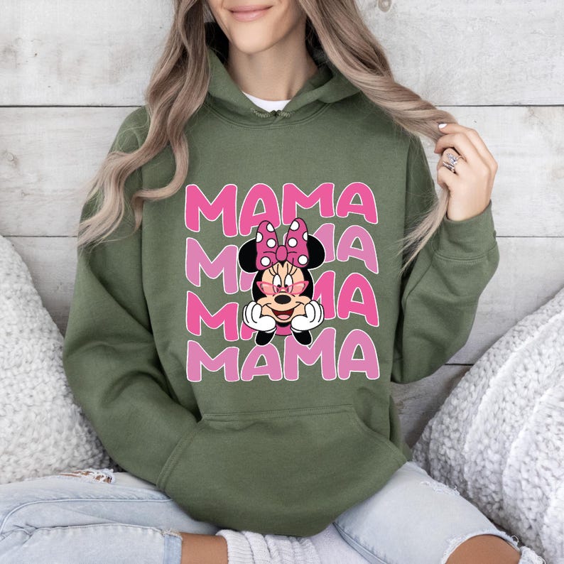 以下が含まれることがあります： ピンクと白のミニーマウスのグラフィックが描かれた緑色のフード付きスウェットシャツ。ミニーマウスはサングラスをかけており、「MAMA」という文字が4回繰り返されています。