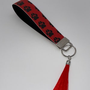 Può includere: Portachiavi rosso e nero con motivo a impronte di zampa e un pon pon rosso.