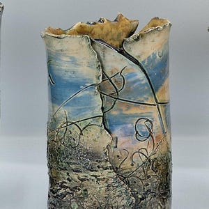 May include: A cylindrical ceramic vase with a textured surface and a cracked design. The vase features a colour palette of blue, beige, and brown, with intricate line details. The top edge has a unique, uneven shape.