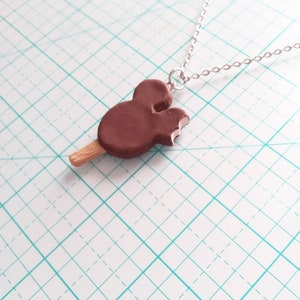 May include: A brown chocolate Mickey Mouse ice cream bar charm on a silver chain necklace.