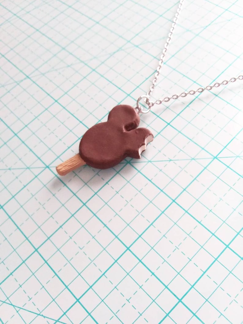 May include: A brown chocolate Mickey Mouse ice cream bar charm on a silver chain necklace.