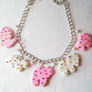 May include: A silver chain necklace with five pink and white sprinkle-covered cookie charms. The charms are shaped like a heart and a bear.