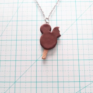 May include: A silver chain necklace with a brown chocolate Mickey Mouse popsicle pendant.