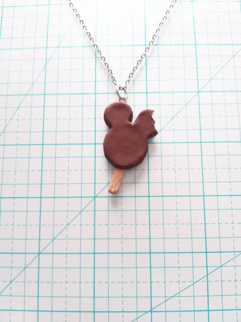 May include: A silver chain necklace with a brown chocolate Mickey Mouse popsicle pendant.